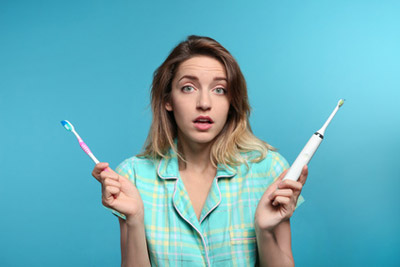 junge Frau weiß nicht, ob Sie eine elektrische oder eine herkömmliche Zahnbürste wählen soll.